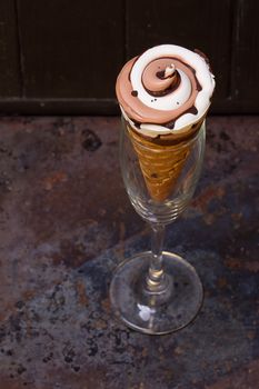 Ice cream in waffle cone with chocolate syrup toppingn in glass on dark black background