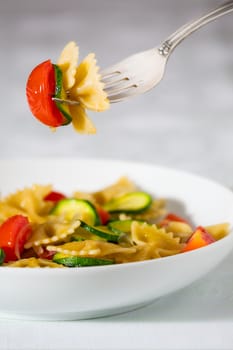 Whole farfalle pasta with zucchini, cherry tomatoes and red onion suspended on the fork
