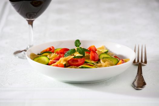 Whole farfalle pasta with zucchini, cherry tomatoes and red onion with a red wine glass