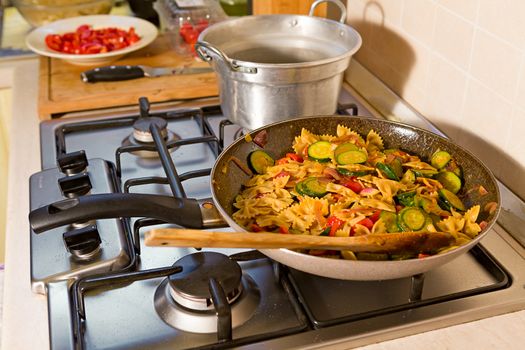 Whole farfalle pasta, zucchini, cherry tomatoes and red onion cooking in the pan