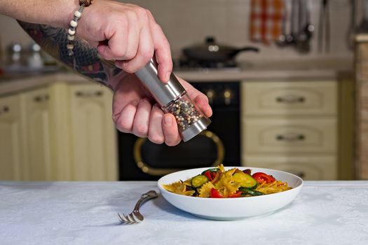 Whole farfalle pasta with zucchini, cherry tomatoes and red onion and a man with pepper grinder on it