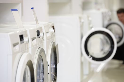 Washing machines, dryer and other domestic appliance equipment in the store. focus at equipment, defocused unrecognizable customer at background.