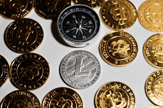 Cryptocurrency physical metal Litecoin coin on gold bitcoin coins near compass. Money concept.