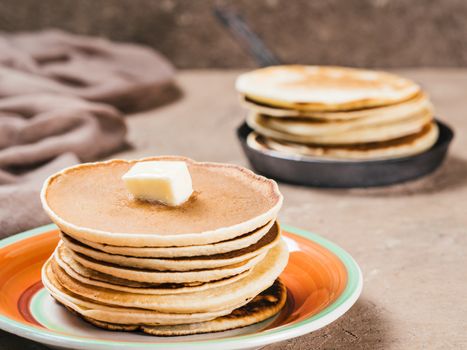Close up view of homemade pancakes. Stack of pancakes with butter on brown concrete background.