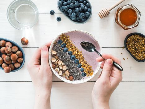 Eating healthy breakfast bowl. Buckwheat smoothie porrige, fresh berries, seeds and nuts, bee pollen in white ceramic bowl in woman hands on table. Clean eating, dieting,detox, vegetarian food concept