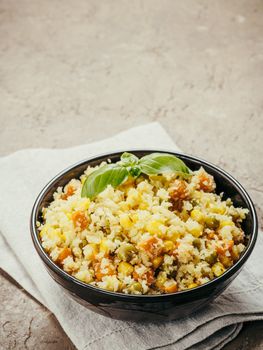 Close up view of cauliflower rice with vegetables. Organic paleo Cauliflower Rice with corn, green peas and carrots on brown concrete background. Copy space.