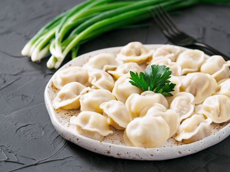 Traditional russian pelmeni, ravioli, dumplings with meat on black concrete background. Russian food and russian kitchen concept.