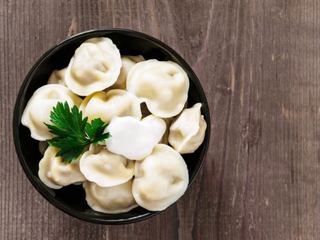 Close up viw of traditional russian pelmeni, ravioli, dumplings with meat on brown wooden background. Copyspace. Top view or flat lay. Russian food and russian kitchen concept.