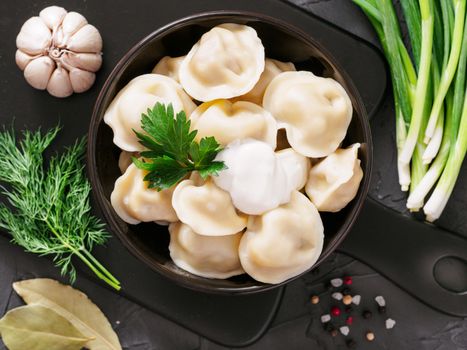 Traditional russian pelmeni, ravioli, dumplings with meat on black concrete background. Top view or flat lay. Russian food and russian kitchen concept.