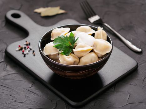 Traditional russian pelmeni, ravioli, dumplings with meat on black cutting board over black concrete background. Russian food and russian kitchen concept.