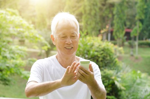 Portrait of happy gray hair Asian old man using smart phone, sitting at outdoor park in morning. 