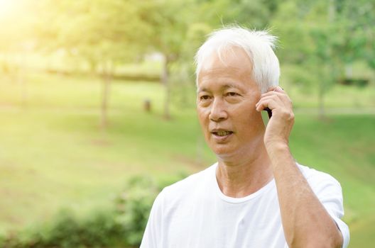 Portrait of gray hair Asian old man calling on smart phone, standing at outdoor park in morning. 