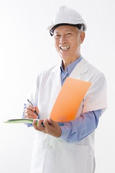 Portrait of old Asian man in uniform with hard hat writing, standing isolated on white background.