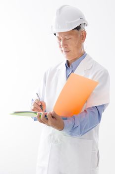 Portrait of old Asian contractor in uniform with hard hat writing, standing isolated on white background.