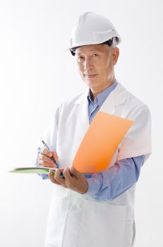 Portrait of old Asian technician in uniform with hard hat writing, standing isolated on white background.