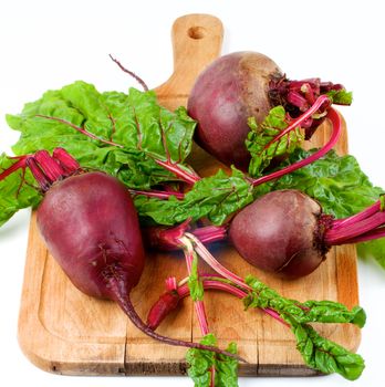 Arrangement of Fresh Raw Organic Beet Roots Full Body and Young Sprouts with Green Beet Tops on Wooden Cutting Board on White background