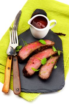 Slices of Roast Beef Medium Rare on Slate Serving Board with Tomato Sauce, Fork and Table Knife on Green Napkin closeup