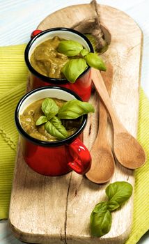 Delicious Vegan Cream Soup in Soup Cups with Wooden Spoons with Basil on Serving Board closeup on Wooden background