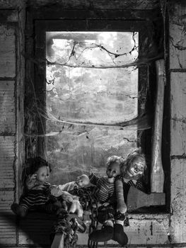 Photo of old dolls and an axe resting on an old window ledge covered in spiderwebs and dust.
