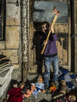 Photo of an axe swinging young boy standing over old dolls and in a barn covered in spiderwebs and dust.