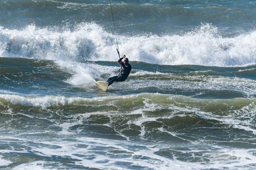 Kitesurfer riding ocean waves on a bright sunny day.