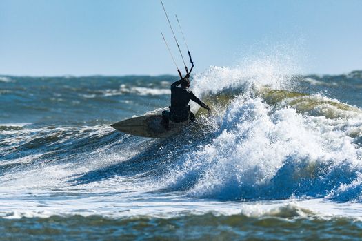 Kitesurfer riding ocean waves on a bright sunny day.