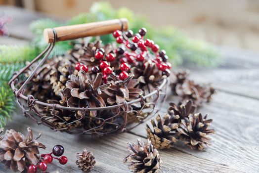 Christmas concept: full basket of pine cones and red holly berries and spruce branches on the background of old unpainted wooden boards. Christmas wallpaper