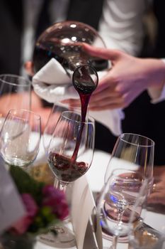 Sommelier pouring wine into glass from mixing bowl at luxury diner