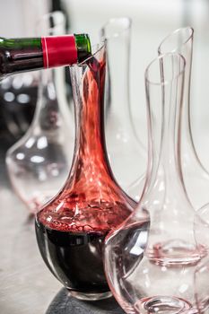 Sommelier at work, pouring wine to decanter while standing near the wine shelf, Luxury Diner