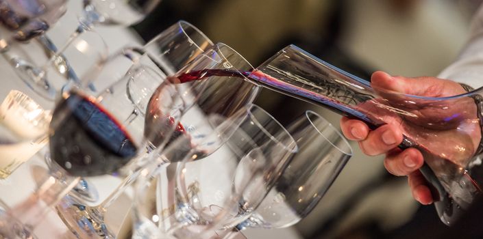 Sommelier pouring wine into glass from mixing bowl at luxury diner