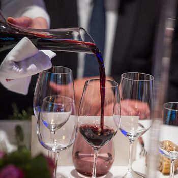 Sommelier pouring wine into glass from mixing bowl at luxury diner