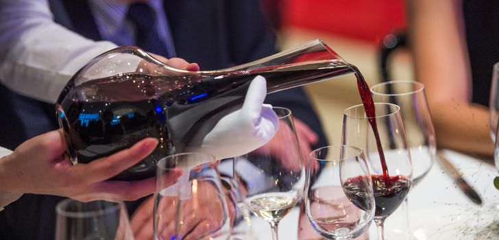 Sommelier pouring wine into glass from mixing bowl at luxury diner