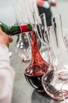 Sommelier at work, pouring wine to decanter while standing near the wine shelf, Luxury Diner