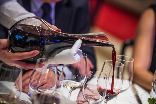 Sommelier pouring wine into glass from mixing bowl at luxury diner