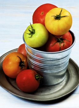 Arrangement of Colorful Fresh Tomatoes with Water Drops in Tin Bucket on Tin Plate closeup on Wooden background
