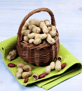 Arrangement of Fresh Peanuts with Nutshell in Wicker Basket on Green Napkin closeup on Wooden background