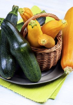 Arrangement of Green and Yellow Fresh Ripe Zucchini in Wicker Basket on Tin Plate closeup on Wooden background
