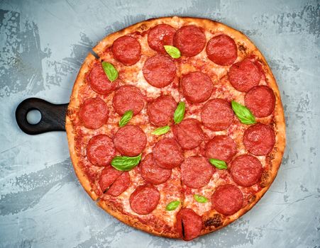 Freshly Baked Pepperoni Pizza with Tomatoes, Pepperoni, Cheese and Basil on Cutting Board on Grey Textured background. Top View