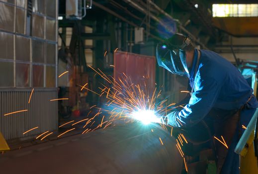 Welder performs welding large diameter pipe inside plant