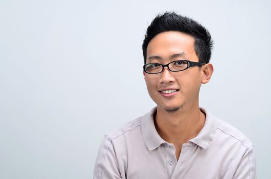 Portrait of Asian man smiling and looking at camera, standing isolated on plain background.