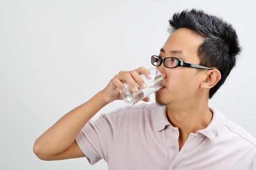 Portrait of Asian man hand holding glass drinking mineral water, standing isolated on plain background.