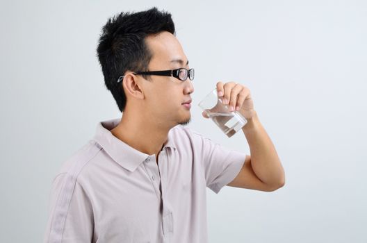 Portrait of Asian man drinking mineral water, standing isolated on plain background.
