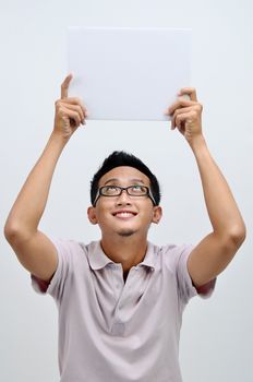 Portrait of happy Asian man hand holding white blank paper card above his head, standing isolated on plain background.