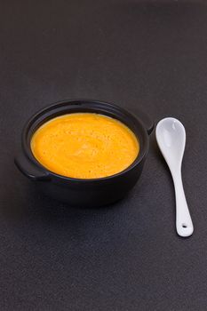 Pumpkin and carrot soup with cream and parsley on dark background