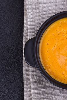 Pumpkin and carrot soup with cream and parsley on dark background