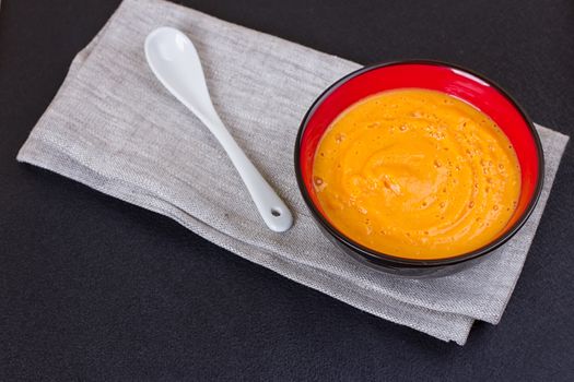 Pumpkin and carrot soup with cream and parsley on dark wooden background