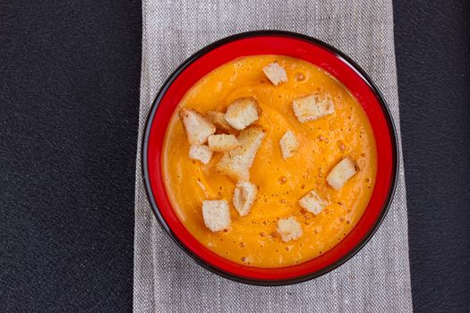 Pumpkin and carrot soup with cream and parsley on dark background Copy space