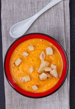 Pumpkin and carrot soup with cream and parsley on dark background