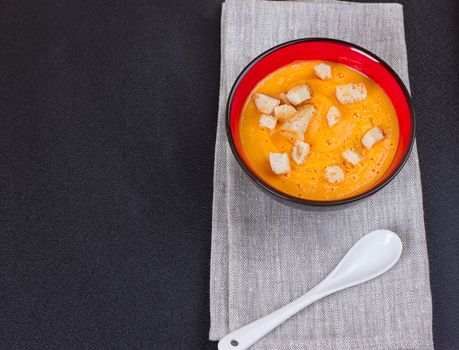 Pumpkin and carrot soup with cream and parsley on dark background Copy space