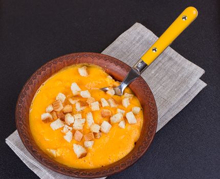 Pumpkin and carrot soup with cream and parsley on dark background Copy space